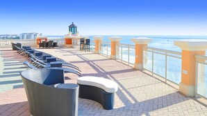 A sunlit outdoor seating area with wicker chairs and a small table, overlooking a clear blue sea. - Gulf-view condo with beach access, pool, hot tub, sauna, & private balcony (Destin)