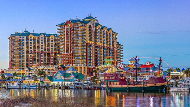 A multi-story hotel with balconies, located near a waterfront with boats docked. - Gulf-view condo with beach access, pool, hot tub, sauna, & private balcony (Destin)