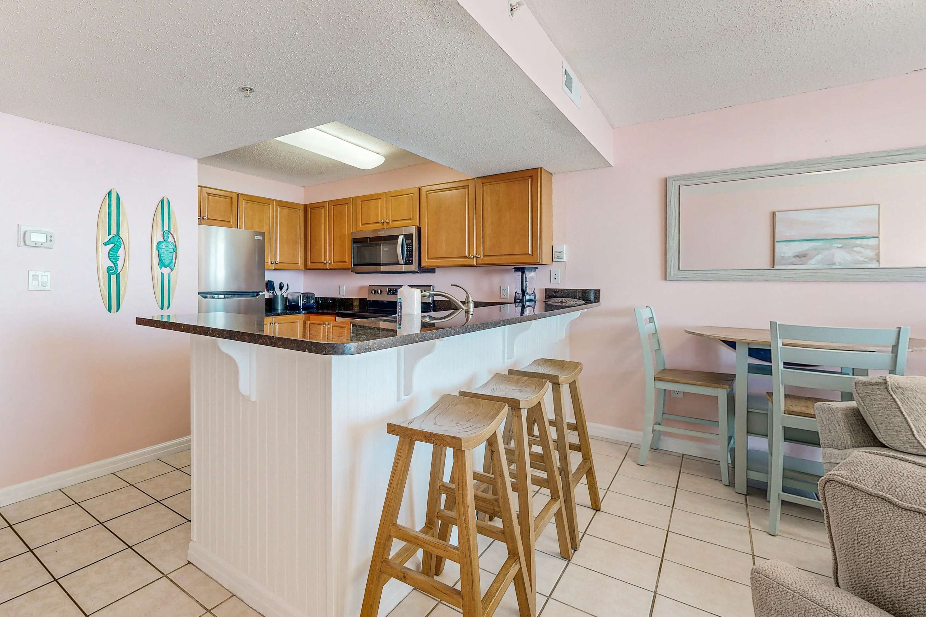 A kitchen with wooden cabinets, a stainless steel refrigerator, a microwave, and a bar stool area.