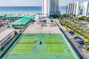 Un court de tennis avec un parking et une vue sur l’océan.
