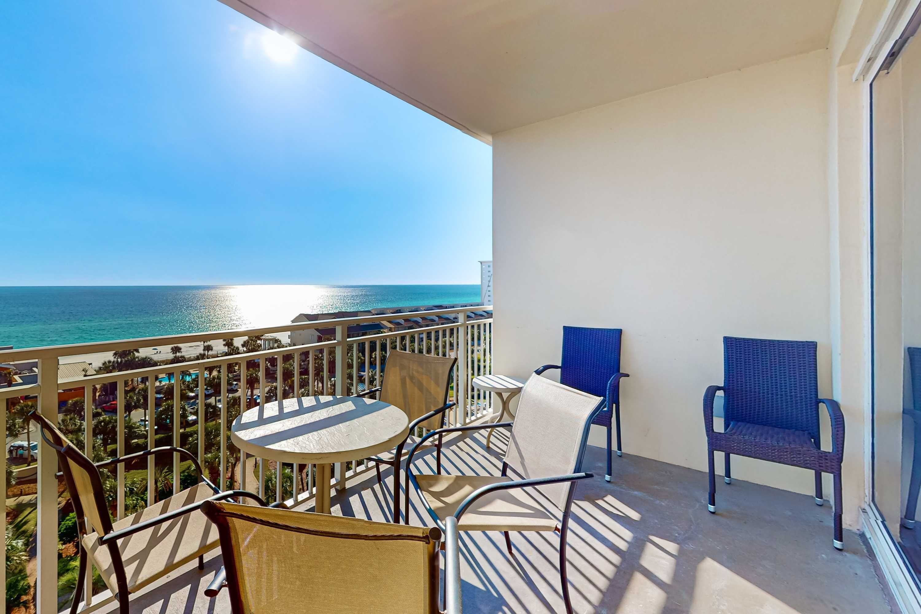 Een balkon met uitzicht op de oceaan, met een ronde tafel en stoelen, en een blauwe stoel.