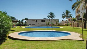 A swimming pool area with two pools, surrounded by well-maintained grass and palm trees, with a building in the background. - Sunlit Marbella Apartment Near Sea (Marbella)