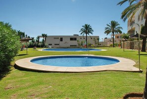 A swimming pool area with two pools, surrounded by well-maintained grass and palm trees, with a building in the background. - Sunlit Marbella Apartment Near Sea (Marbella)