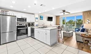 A modern kitchen with stainless steel appliances, a central island, and a dining area with a view. - Gorgeous 2nd-floor condo with W&D, resort style pool, gym, and beach access (Destin)
