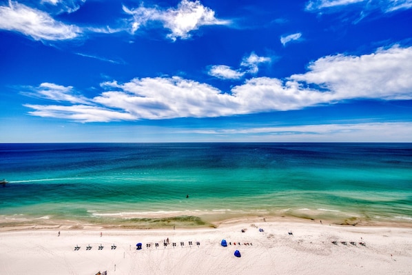 A beach with clear turquoise waters, a sandy shore, and a few umbrellas. - 8th-floor condo with balcony, ocean view, W&D, pools & hot tub (Destin)