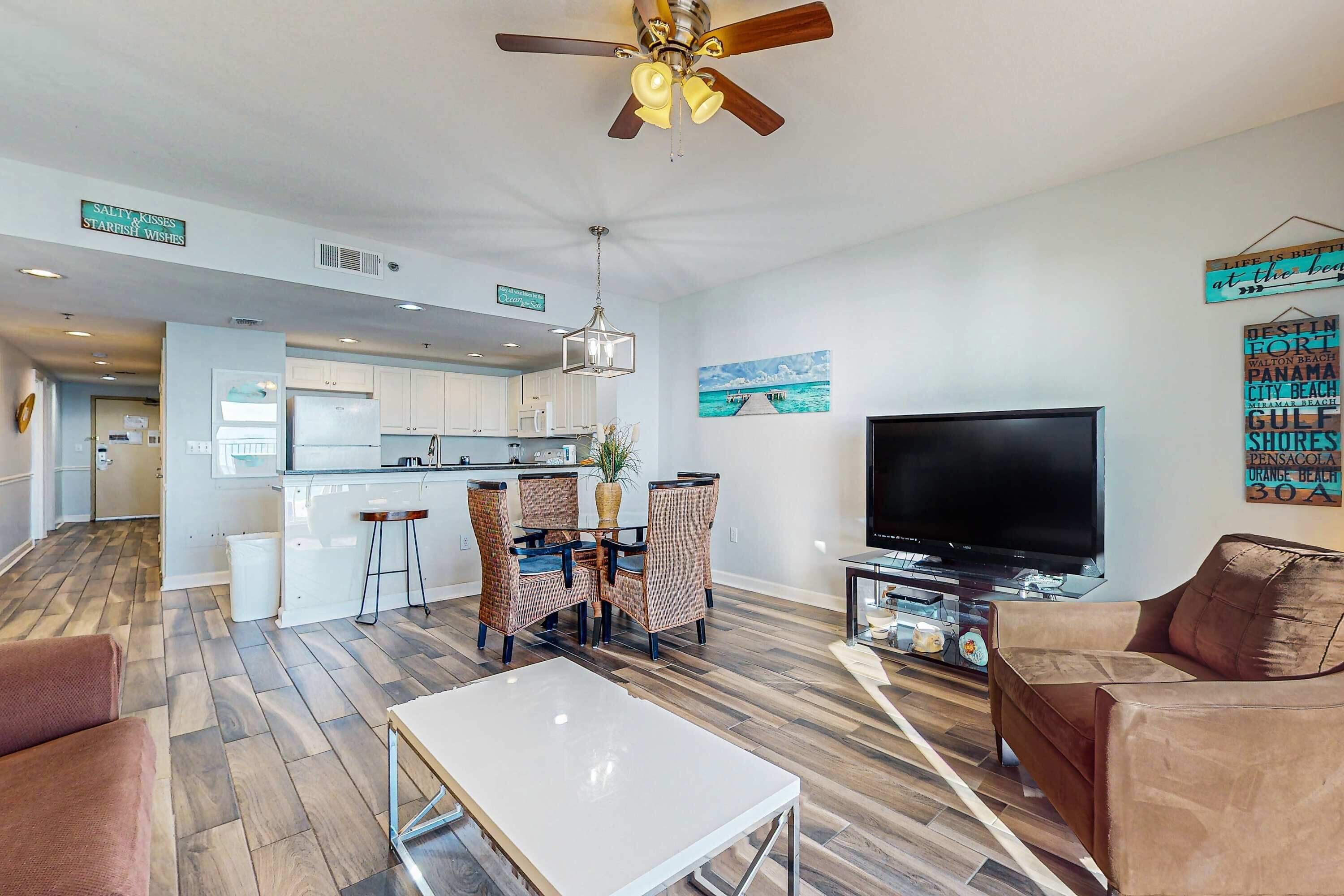 A modern living room with a flat-screen TV, a ceiling fan, and a dining area with wicker chairs.