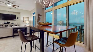 A modern living room with a dining table, two chairs, a sofa, a television, and a large window with a view of the outdoors. - Spacious penthouse condo and private balcony, shared pool&fitness, beach access (Destin)