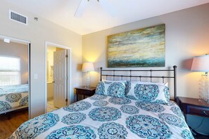 Une chambre à coucher avec un lit, des lampes de chevet, un tableau au mur et une porte donnant sur une autre pièce.