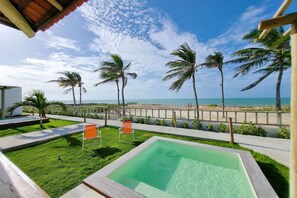 Zona de piscina con vista a la playa, palmeras y cielo despejado.
