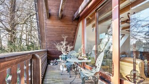 Una terraza de madera con mobiliario exterior, incluyendo una mesa y sillas, y barandilla de madera.