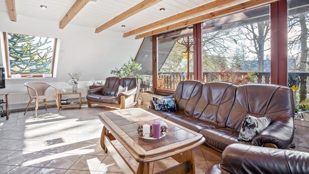 Un salón espacioso con techo de madera, ventanas amplias, un sofá de cuero marrón y una mesa de centro.