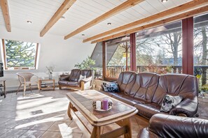 A spacious living room with a wooden ceiling, large windows, a brown leather sofa, and a coffee table. - Apartment C with Sea View, Private Terrace, and Wi-Fi (Klausdorf)