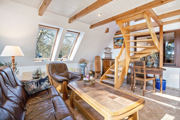 Ein gemütliches Wohnzimmer mit einer Holztreppe, Ledermöbeln und großen Fenstern.