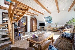 Ein großzügiger Wohnbereich mit einer Holztreppe, einem Fernseher, einem Sofa und einem Esstisch.