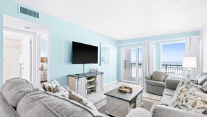 A living room with a sofa, armchairs, a coffee table, and a TV. There is a window with curtains and a view outside. - Bright third-floor Gulf-front condo directly on the beach with amazing views (Fort Walton Beach)