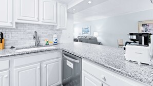 A modern kitchen with white cabinets, a granite countertop, and a built-in dishwasher. - Bright third-floor Gulf-front condo directly on the beach with amazing views (Fort Walton Beach)