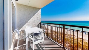 Un balcone con tavolo e sedie bianche, vista su una spiaggia con cielo azzurro e mare turchese.