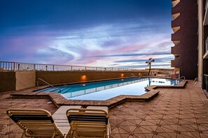 Ein Pool im Freien mit Liegestühlen, einer Palme und Blick auf den Sonnenuntergang.