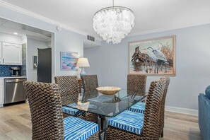 Un coin repas avec une table en verre, des chaises en osier, un lustre et un tableau au mur.