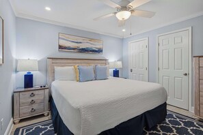 Une chambre à coucher avec un lit, des tables de chevet, un ventilateur de plafond et un tableau accroché au mur.
