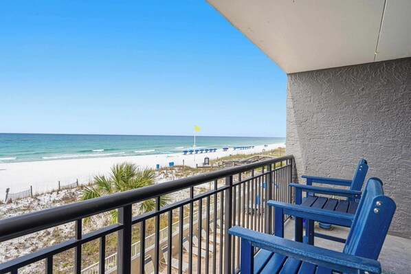 Un balcon avec vue sur la plage, un drapeau et des chaises bleues.