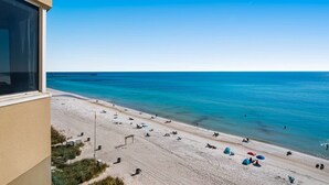 A beach view from a balcony with clear blue water, sandy beach, and a distant pier. - Deluxe, beachfront escape with furnished balcony, pools, hot tub & gym (Panama City Beach)