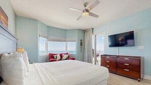 A bedroom with a bed, a ceiling fan, a TV, a dresser, and a window with curtains. - Deluxe, beachfront escape with furnished balcony, pools, hot tub & gym (Panama City Beach)