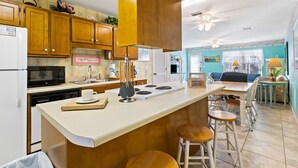 Una cocina con armarios de madera, un refrigerador blanco, un microondas y una estufa. Hay un comedor con una mesa y sillas.