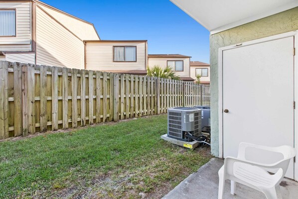 A residential area with a wooden fence, a grassy yard, and a white door. - Bright Condo with Shared Pool, WiFi, Central AC, and Private Patio (Panama City Beach)