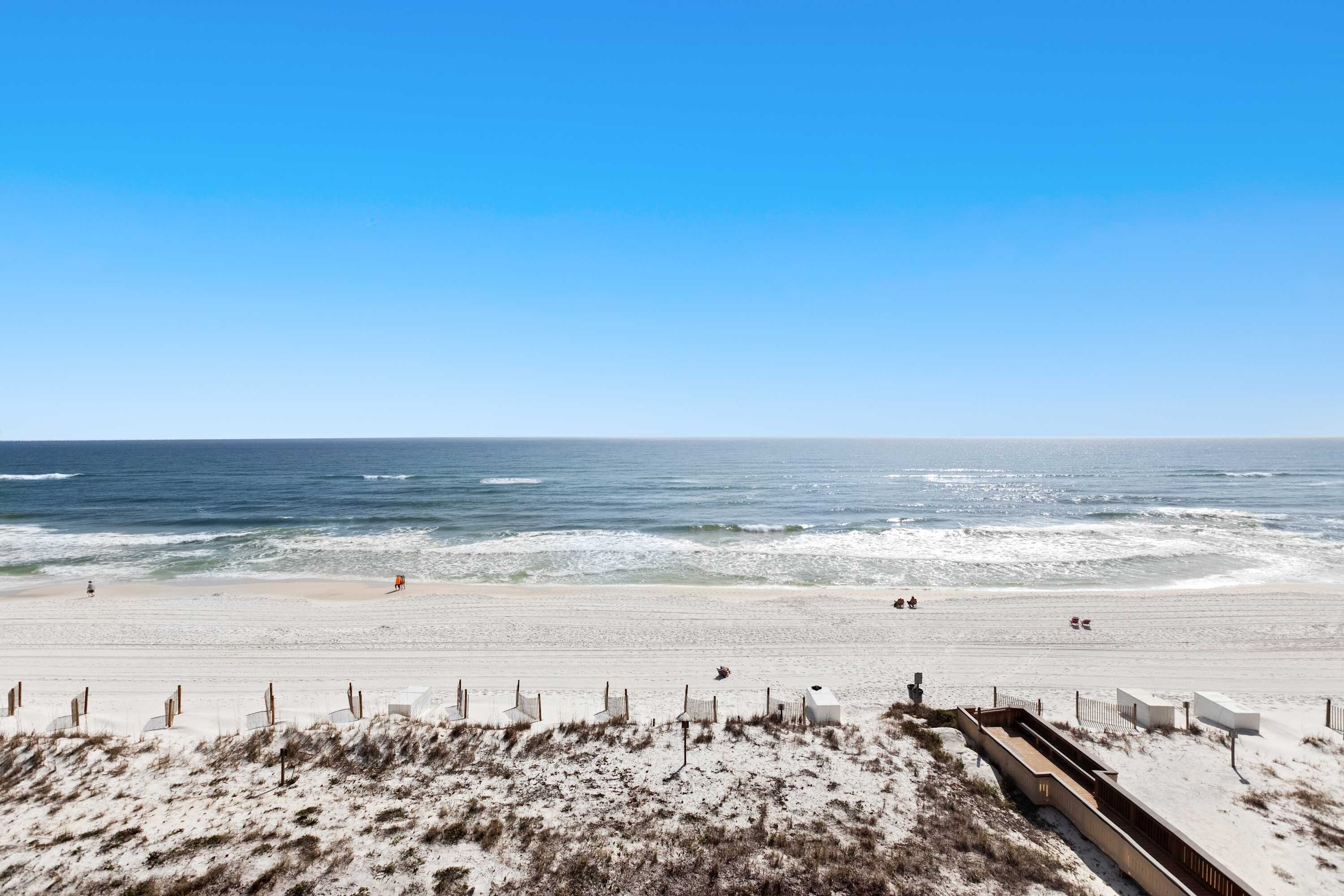 Ein Strand mit sandigem Ufer, einigen Personen und blauem Himmel.