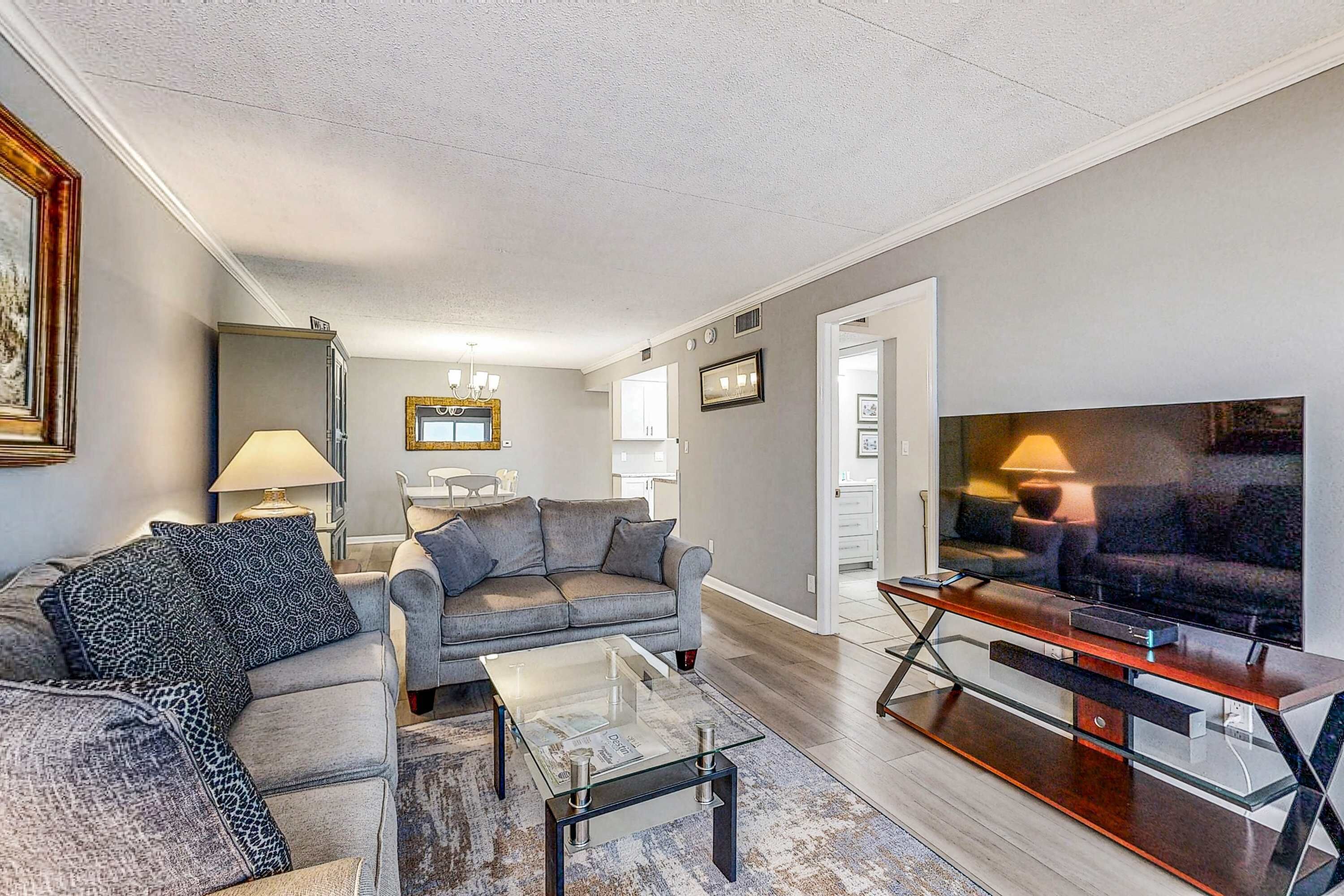 A modern living room with a grey sofa, a glass coffee table, and a flat-screen TV.
