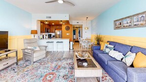 Un salon avec un canapé bleu, une table basse, un téléviseur et un tapis à motifs.