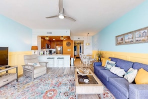 A living room with a blue sofa, a coffee table, a TV, and a patterned rug. - Colorful, waterfront condo with pools, gym, & beach access (Panama City Beach)