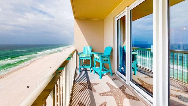 Un balcon donnant sur la plage, deux chaises turquoise et un tapis de sol orné de motifs d’étoiles de mer.