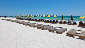 Une plage bordée de rangées de transats et de parasols, un ciel dégagé et l’océan en toile de fond.