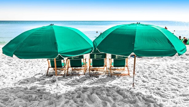 Des chaises de plage avec des parasols verts, sur une plage de sable.
