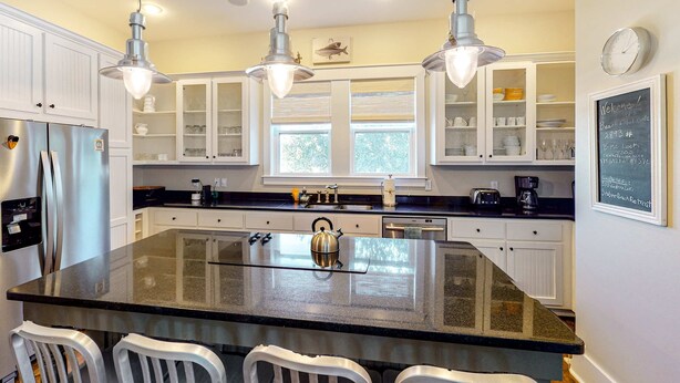 Una cocina moderna con una isla central, electrodomésticos de acero inoxidable, armarios blancos e iluminación colgante.