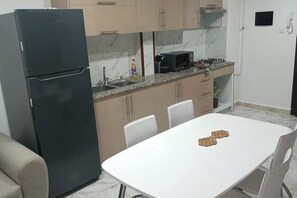 A compact kitchen with a refrigerator, microwave, sink, and a white dining table with chairs. - Honeycomb apartment (Béjaïa)