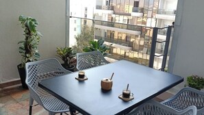 A balcony with a table and chairs, potted plants, and a view of buildings. - Honeycomb apartment (Béjaïa)
