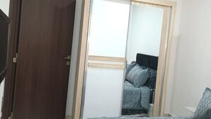 A bedroom with a wooden wardrobe, a bed with patterned bedding, and a mirror cabinet. - Honeycomb apartment (Béjaïa)