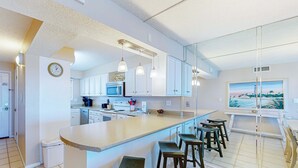 Eine moderne Küche mit weißen Schränken, einer großen Kochinsel mit Barhocker, einer Mikrowelle und einem Landschaftsbild.