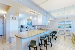 A modern kitchen with white cabinets, a large island with bar stools, a microwave, and a painting of a landscape. - Stunning beachfront condo w/ beach access, shared pool, & private balcony (Panama City Beach)