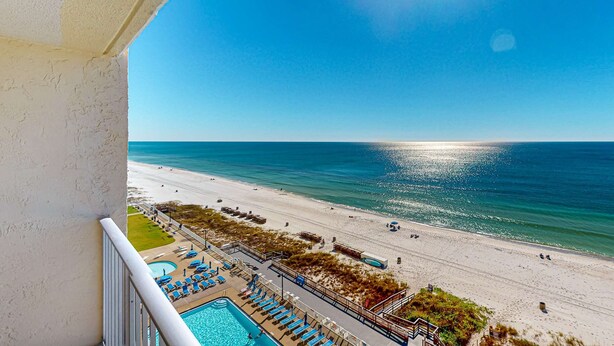 Ein Balkon mit Pool und Liegestühlen mit Blick auf einen Strand und den Ozean.