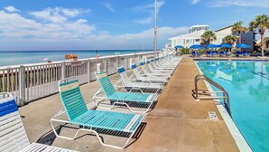 Ein Poolbereich mit Liegestühlen und Sonnenschirmen, Blick auf das Meer und ein Gebäude im Hintergrund.