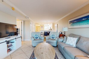 A living room with a sofa, two armchairs, a coffee table, and a TV. There is a kitchen in the background with a dining table and chairs. - Amazing Gulf-Front View On Okaloosa Island, On-Site Pool, Walk-In Shower (Fort Walton Beach)