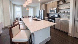 A modern kitchen with a central island, stainless steel appliances, and pendant lighting. - Pool-view condo with on-site pool, hot tub, roof deck, gym, & balcony (Inlet Beach)