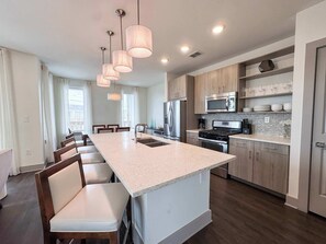 A modern kitchen with a central island, stainless steel appliances, and pendant lighting. - Pool-view condo with on-site pool, hot tub, roof deck, gym, & balcony (Inlet Beach)