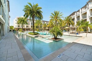 A swimming pool with palm trees, a 3ft depth marker, and a building with balconies. - Pool-view condo with on-site pool, hot tub, roof deck, gym, & balcony (Inlet Beach)