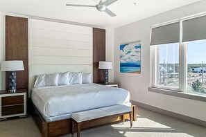 A bedroom with a bed, bedside tables, a ceiling fan, a window with a view, and a painting on the wall. - Pool-view condo with on-site pool, hot tub, roof deck, gym, & balcony (Inlet Beach)