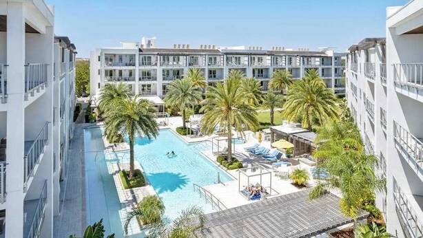 A hotel with a swimming pool surrounded by palm trees and lounge chairs. - Pool-view condo with on-site pool, hot tub, roof deck, gym, & balcony (Inlet Beach)